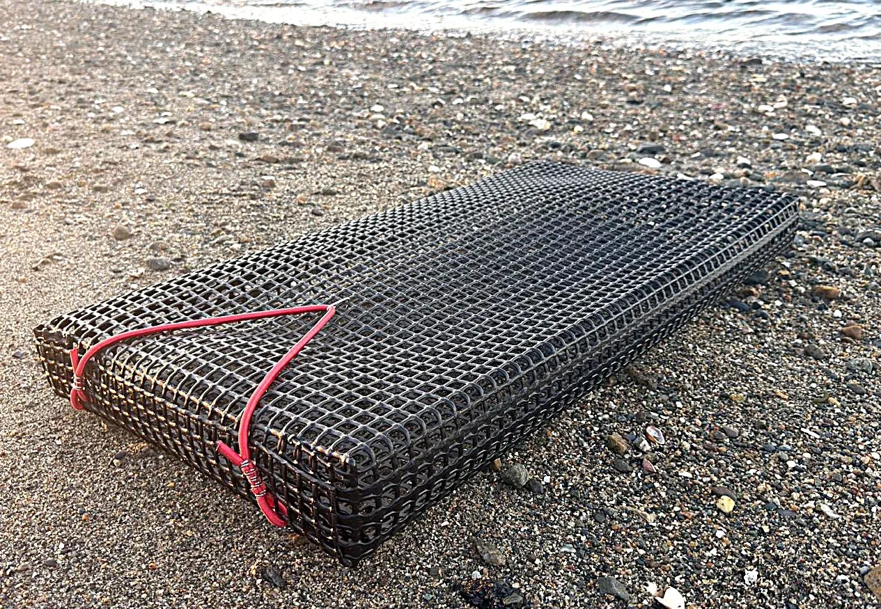 A mesh oyster basket resting on a shoreline after handling